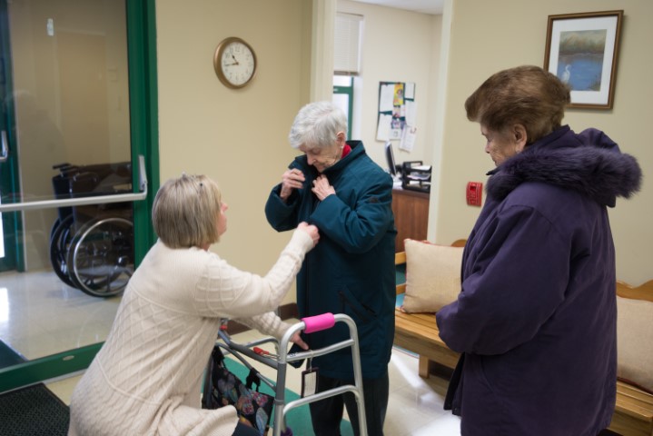 staff at Senior Day Services helping elderly woman put on coat